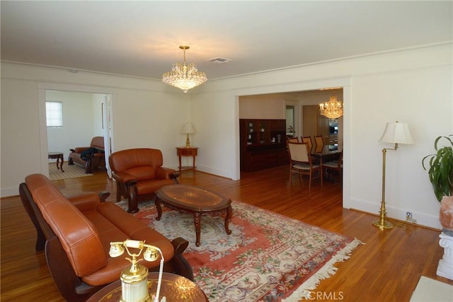 living room with baseboards, an inviting chandelier, wood finished floors, and visible vents