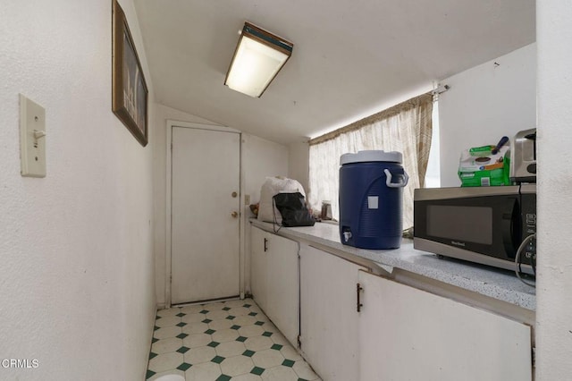 interior space with lofted ceiling, light floors, light countertops, white cabinetry, and stainless steel microwave