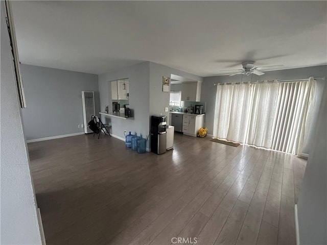 unfurnished living room with dark wood-style flooring, a ceiling fan, and baseboards