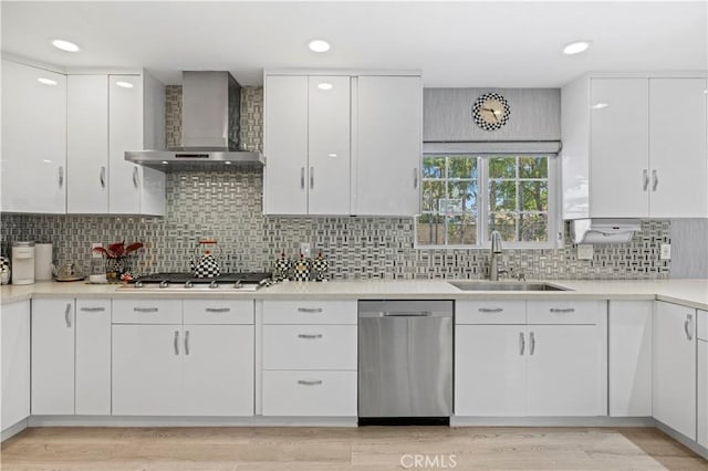 kitchen with a sink, light countertops, white cabinets, stainless steel appliances, and wall chimney exhaust hood