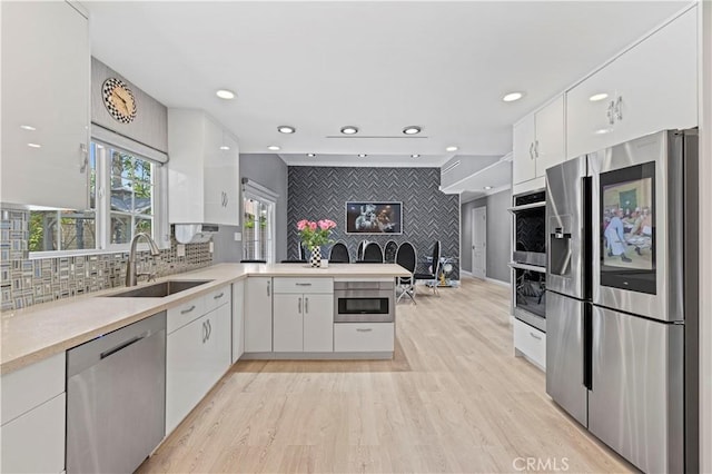kitchen featuring a peninsula, light wood-style floors, white cabinets, a sink, and stainless steel appliances