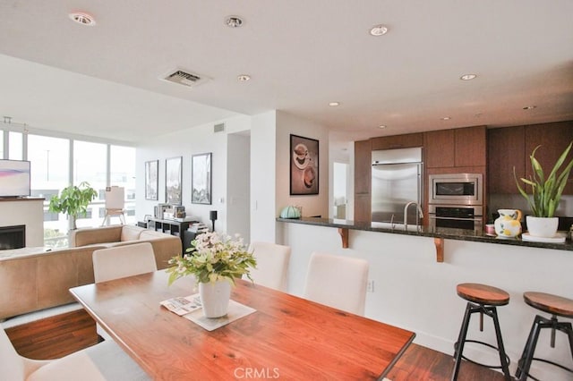 dining space with dark wood-style flooring, visible vents, recessed lighting, and a fireplace
