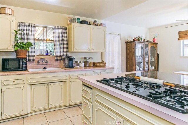 kitchen featuring black microwave, gas cooktop, light countertops, a sink, and light tile patterned floors