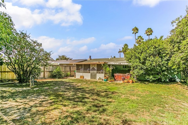 rear view of property with a fenced backyard, a yard, a hot tub, and a sunroom