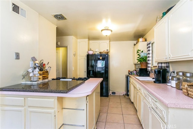kitchen featuring light tile patterned floors, black fridge with ice dispenser, white cabinetry, and visible vents