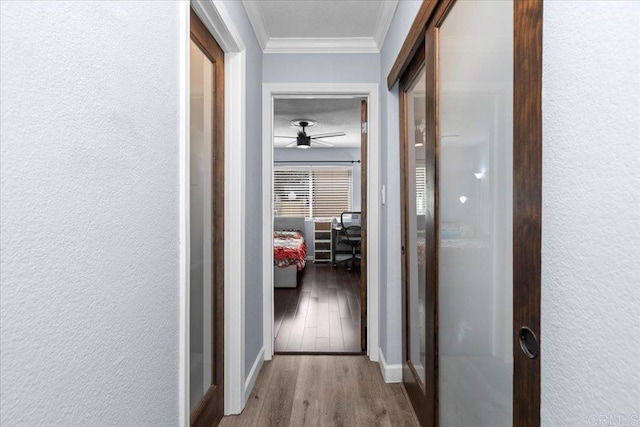 hall featuring baseboards, a textured wall, ornamental molding, and wood finished floors
