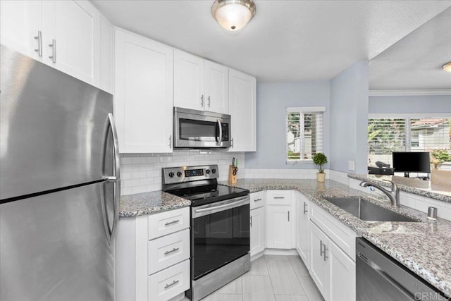 kitchen featuring stainless steel appliances, light stone countertops, white cabinetry, and a sink