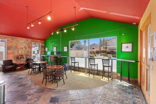 dining area featuring track lighting, lofted ceiling, and stone finish floor