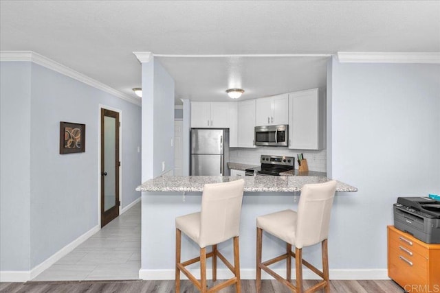 kitchen featuring a breakfast bar area, appliances with stainless steel finishes, tasteful backsplash, a peninsula, and white cabinetry