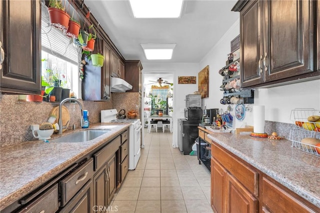 kitchen with white range with gas stovetop, under cabinet range hood, tasteful backsplash, a sink, and light tile patterned floors