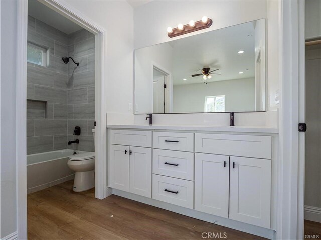 full bath with double vanity, a ceiling fan, wood finished floors, a sink, and toilet