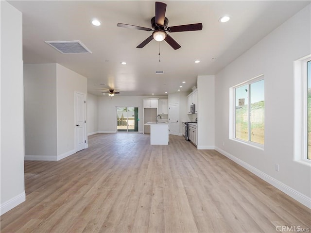 unfurnished living room featuring visible vents, a sink, baseboards, light wood-style floors, and a ceiling fan