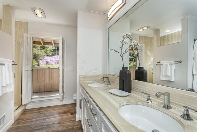 full bath with a sink, toilet, double vanity, and wood finished floors