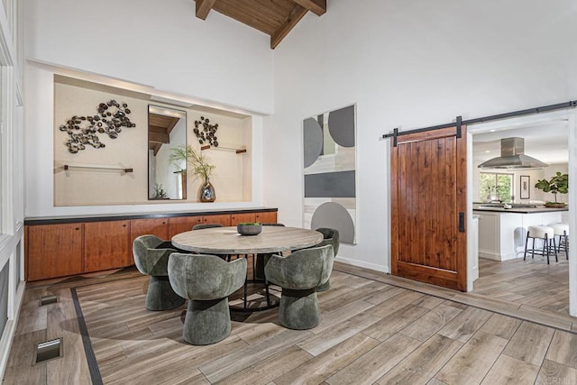 dining space featuring visible vents, beamed ceiling, high vaulted ceiling, a barn door, and light wood-style flooring