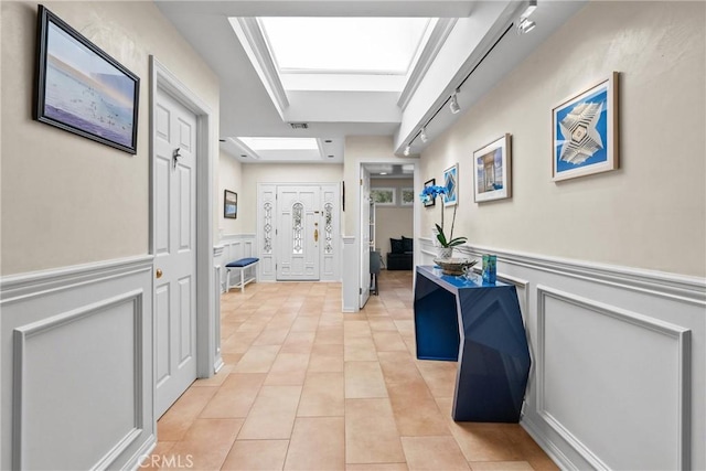 hall featuring light tile patterned floors, a wainscoted wall, and a decorative wall