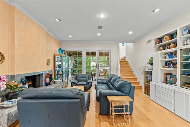 living area featuring crown molding, a high end fireplace, visible vents, and light wood-type flooring