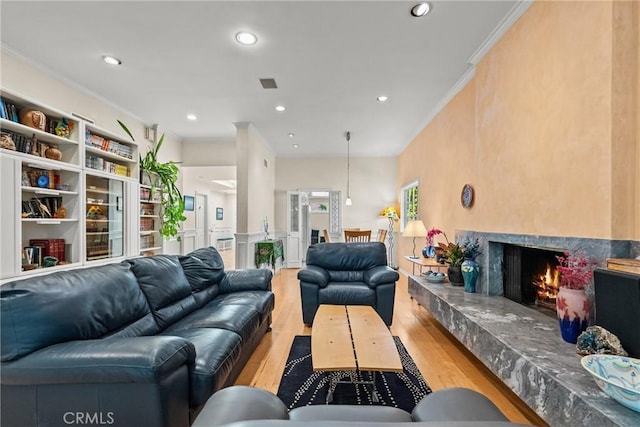 living area featuring wood finished floors, a wainscoted wall, ornamental molding, recessed lighting, and a premium fireplace