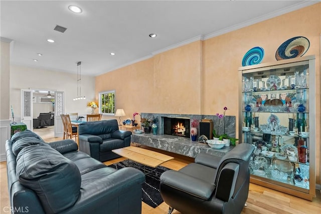 living area with a warm lit fireplace, recessed lighting, light wood-type flooring, visible vents, and ornamental molding