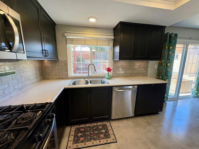 kitchen featuring appliances with stainless steel finishes, a sink, light countertops, dark cabinets, and decorative backsplash