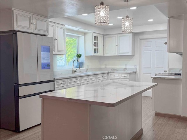kitchen with freestanding refrigerator, white cabinets, light stone counters, and light wood-type flooring