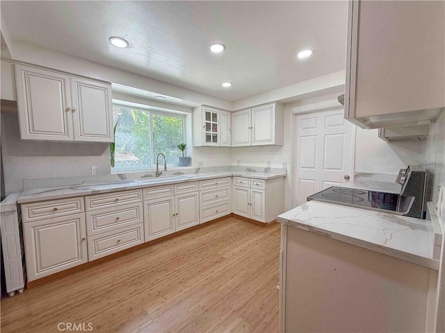 kitchen featuring light stone countertops, stove, light wood-type flooring, recessed lighting, and a sink