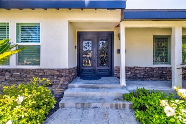 view of exterior entry featuring stucco siding, french doors, and stone siding