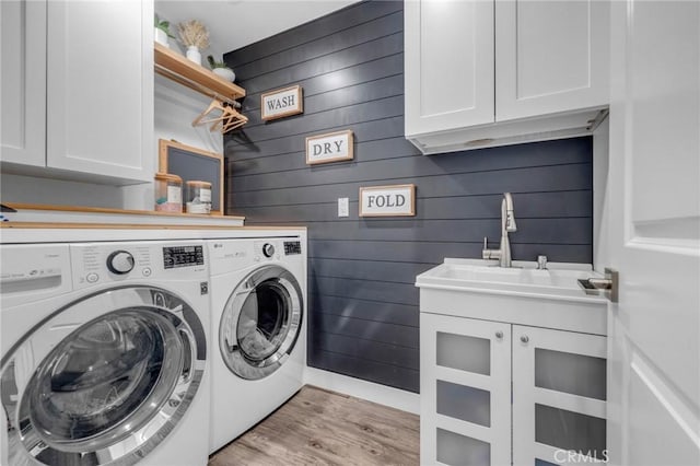 clothes washing area featuring wood walls, light wood-type flooring, separate washer and dryer, a sink, and cabinet space