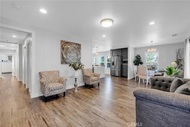 living area with light wood-type flooring, recessed lighting, a chandelier, and a healthy amount of sunlight