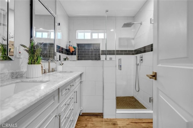 full bath with double vanity, a sink, wood finished floors, and a shower stall