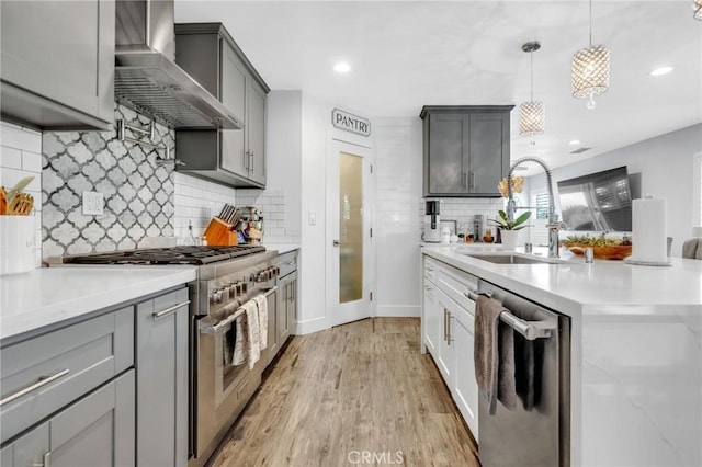 kitchen with wall chimney range hood, appliances with stainless steel finishes, a sink, light wood finished floors, and tasteful backsplash