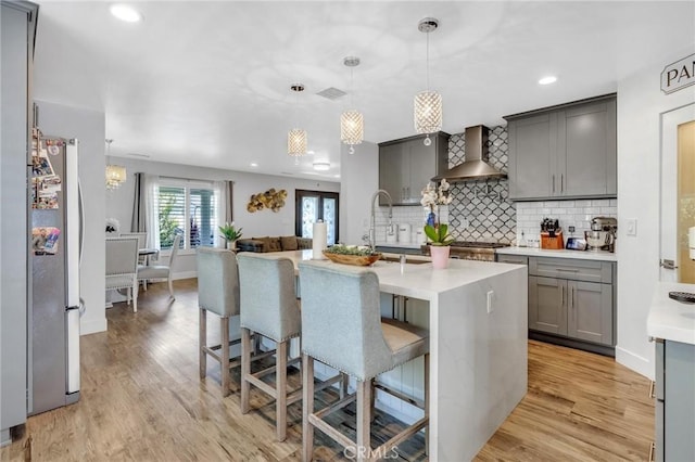 kitchen featuring freestanding refrigerator, light countertops, gray cabinetry, and wall chimney range hood