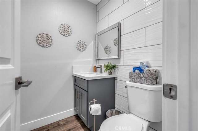 half bathroom featuring baseboards, wood finished floors, toilet, and vanity