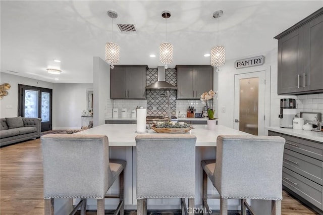 kitchen featuring light countertops, backsplash, wall chimney range hood, and a kitchen bar