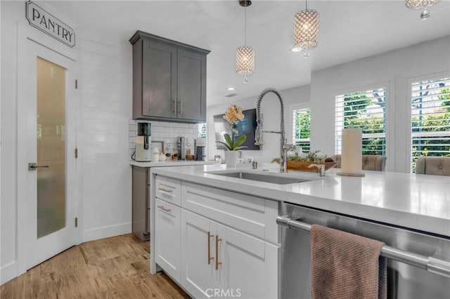 kitchen with stainless steel dishwasher, decorative backsplash, light wood-style floors, light countertops, and a sink