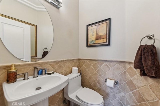 bathroom with a sink, a wainscoted wall, toilet, and tile walls