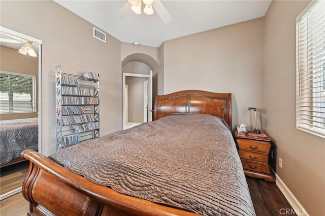 bedroom featuring ceiling fan, visible vents, arched walkways, wood finished floors, and baseboards