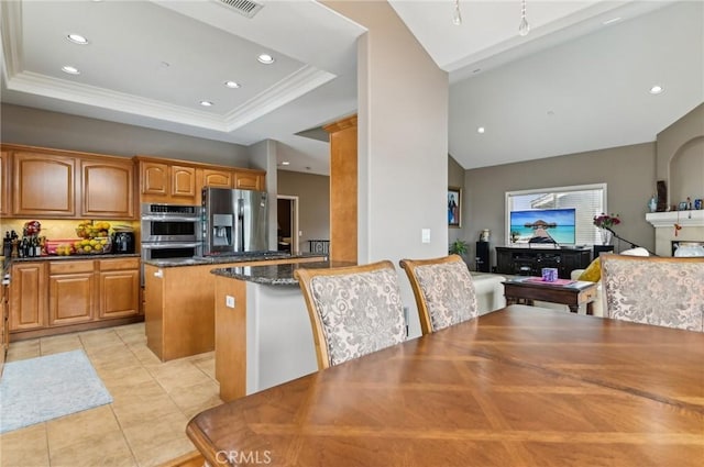 kitchen with light tile patterned flooring, a kitchen island, dark stone counters, appliances with stainless steel finishes, and vaulted ceiling