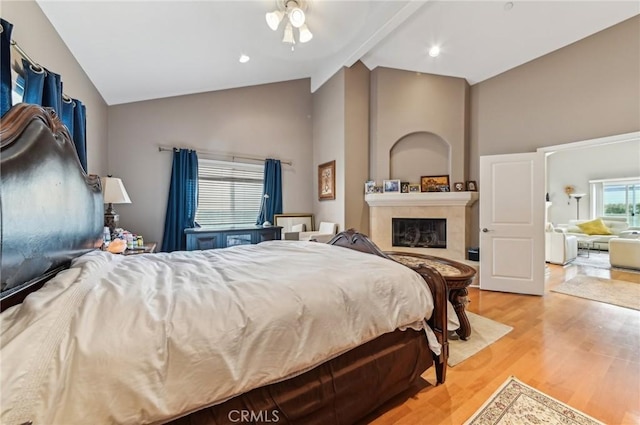 bedroom featuring light wood-style floors, high vaulted ceiling, a fireplace, and beam ceiling