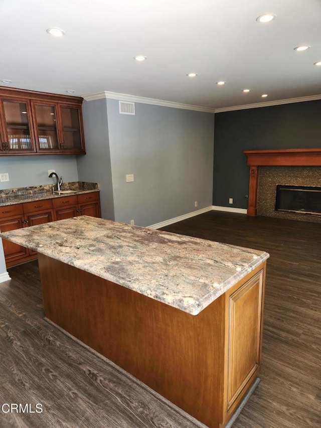 kitchen with dark wood-type flooring, recessed lighting, crown molding, and light stone counters