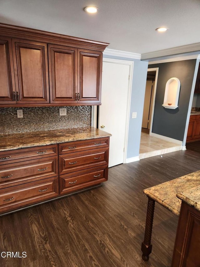 kitchen featuring crown molding, decorative backsplash, stone counters, baseboards, and dark wood finished floors