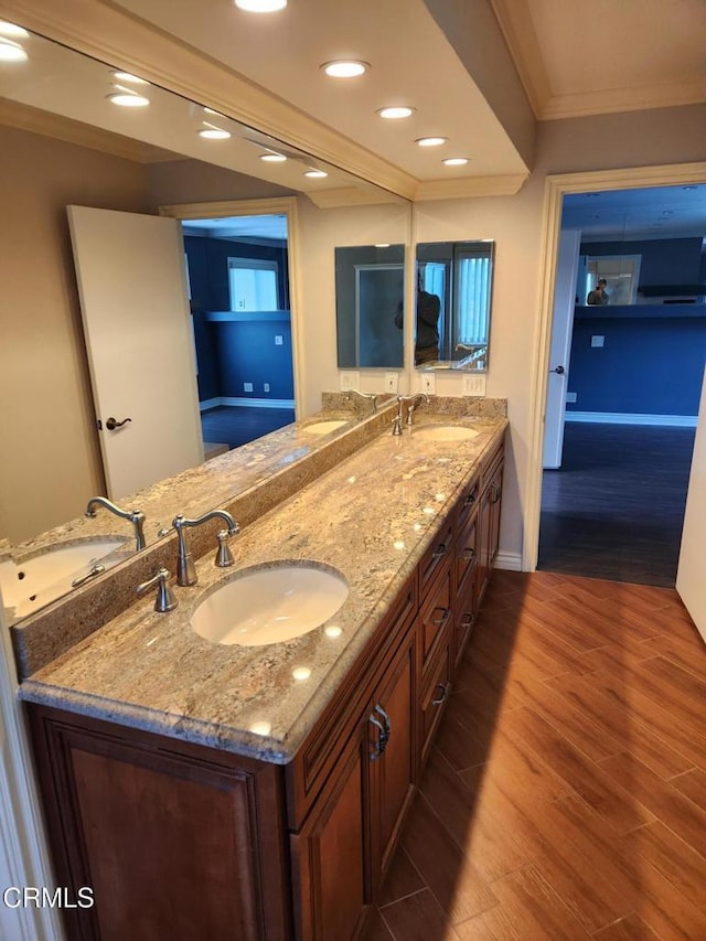 bathroom with a sink, crown molding, double vanity, and wood finished floors