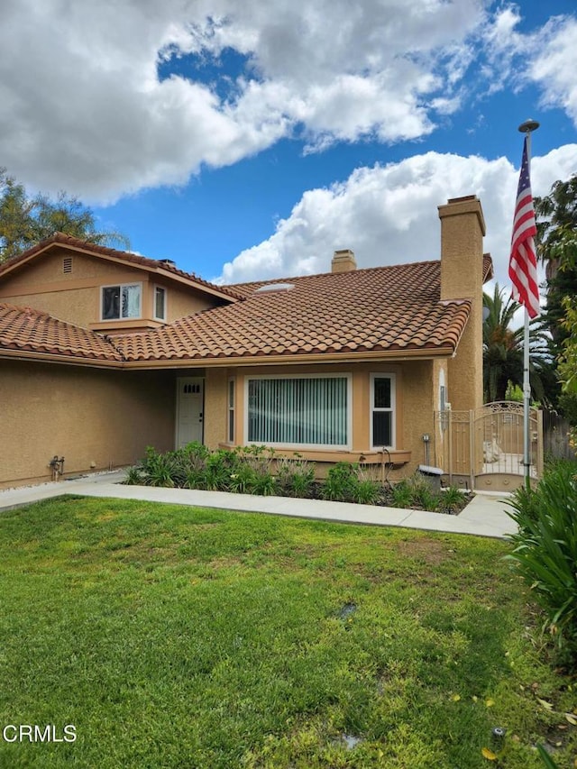 view of front of home featuring a chimney, a gate, a front yard, and stucco siding