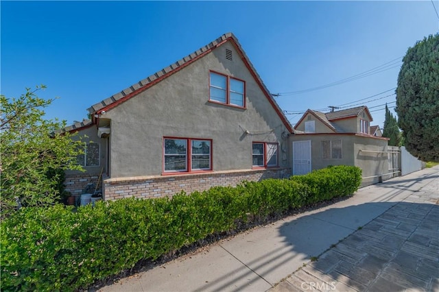 view of side of property featuring a tiled roof, fence, and stucco siding
