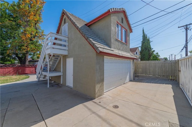 view of side of property with a garage, stucco siding, stairway, and fence