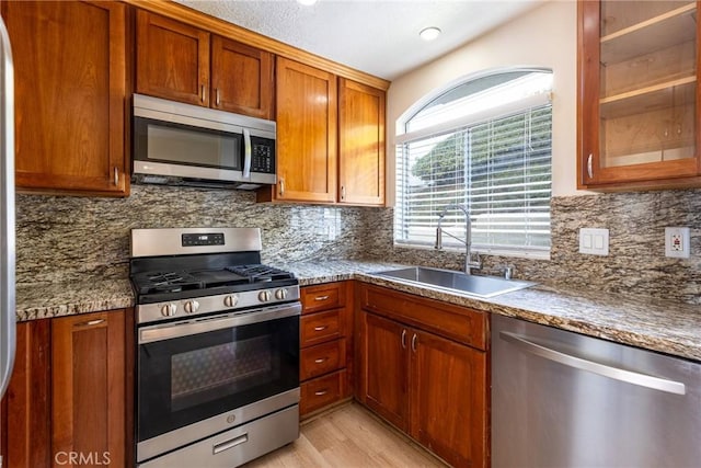 30902 Clubhouse Dr Unit 24E, Laguna Niguel, CA 92677 - kitchen with appliances with stainless steel finishes, a sink, decorative backsplash, brown cabinetry, and light wood finished floors