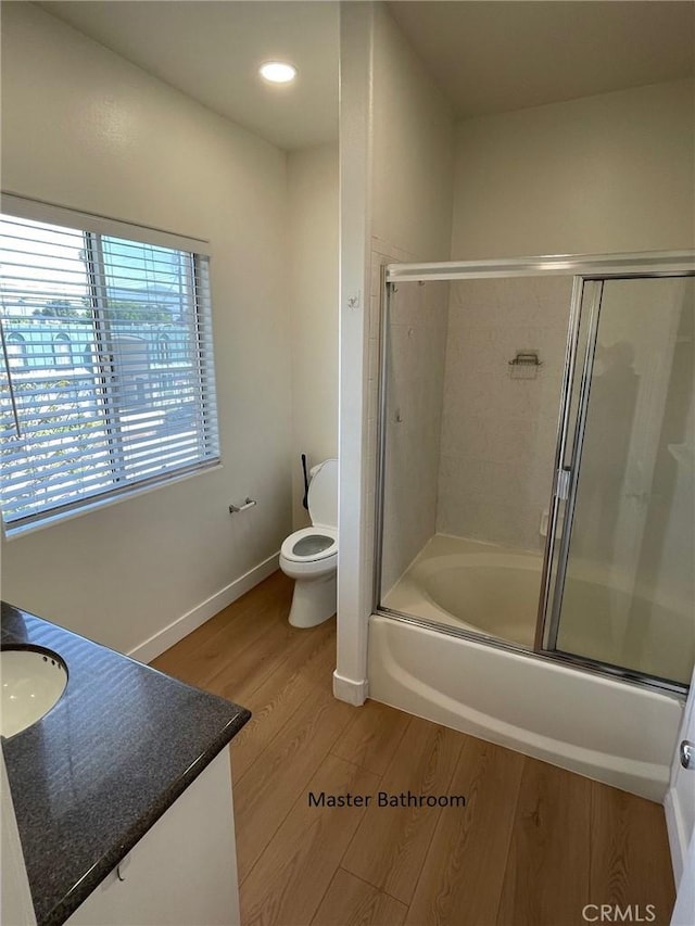 bathroom featuring vanity, wood finished floors, toilet, baseboards, and enclosed tub / shower combo