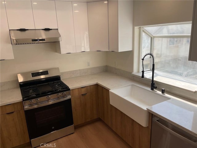 kitchen featuring white cabinets, a sink, wall chimney exhaust hood, stainless steel appliances, and modern cabinets