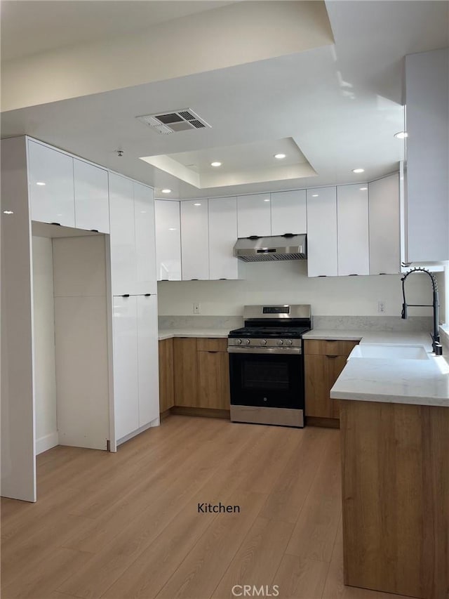 kitchen featuring gas stove, modern cabinets, under cabinet range hood, and visible vents
