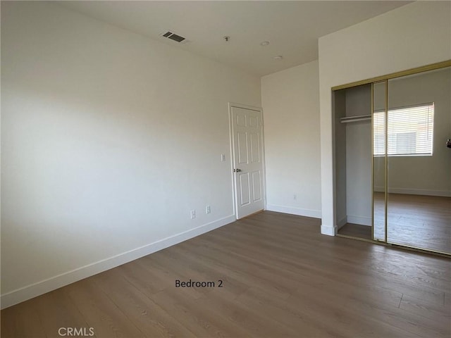 unfurnished bedroom featuring a closet, baseboards, visible vents, and dark wood-type flooring
