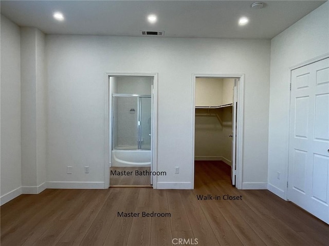 unfurnished bedroom featuring visible vents, wood finished floors, baseboards, a spacious closet, and ensuite bath